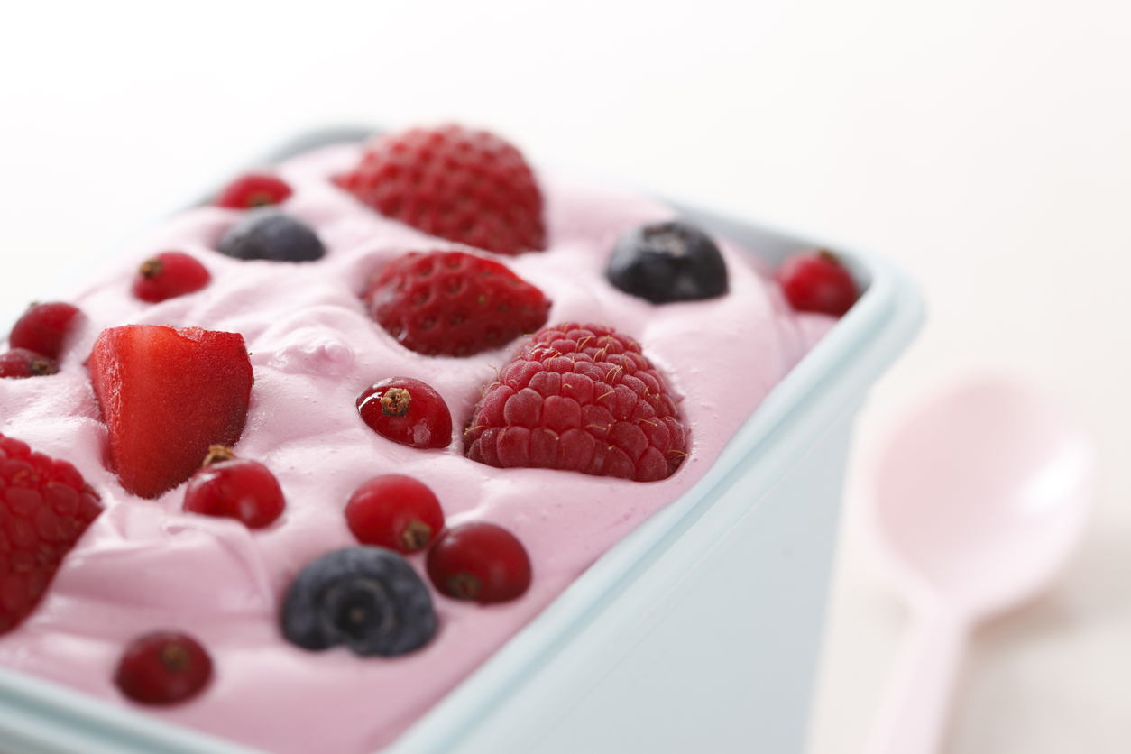 White container with blueberries, strawberries and raspberries in pink yogurt.